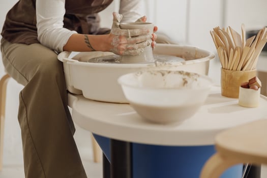 Female potter in apron making shape of clay vase on spinning pottery tool in ceramic workshop photo