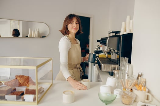 Woman barista in apron pouring hot milk foam into coffee. Professional coffee brewing concept photo
