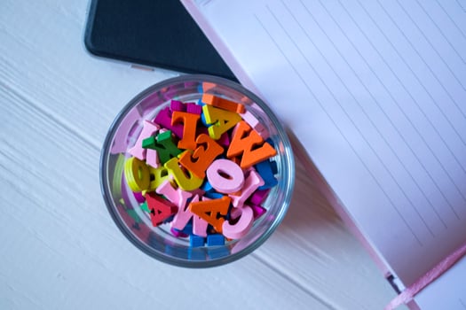 A half of opened notepad and multicolored letters in glass on a white wooden desk. Close up. photo