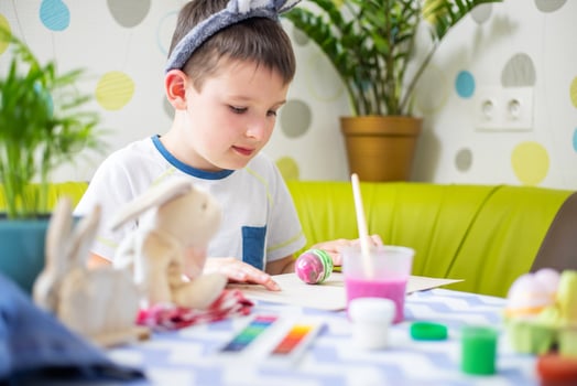 Happy Easter. Boy in bunny ears dyes colorful egg for Easter hunt photo