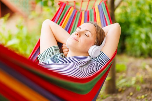 Young woman in headphones listening to music while resting in hammock outdoors photo