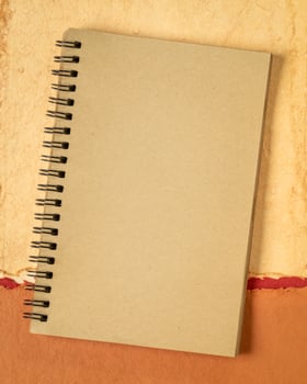 blank spiral notebook against abstract paper landscape, vertical poster photo