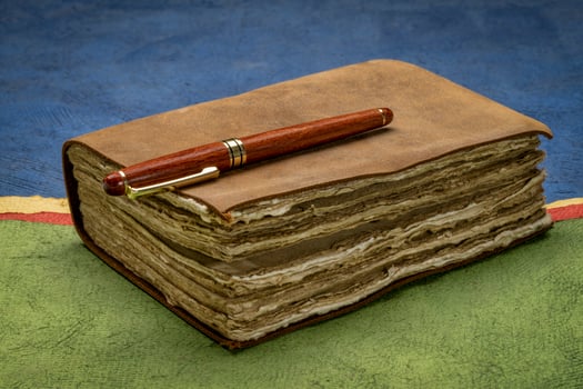 retro leather-bound journal with decked edge handmade paper pages and a stylish pen against abstract paper landscape, journaling concept photo