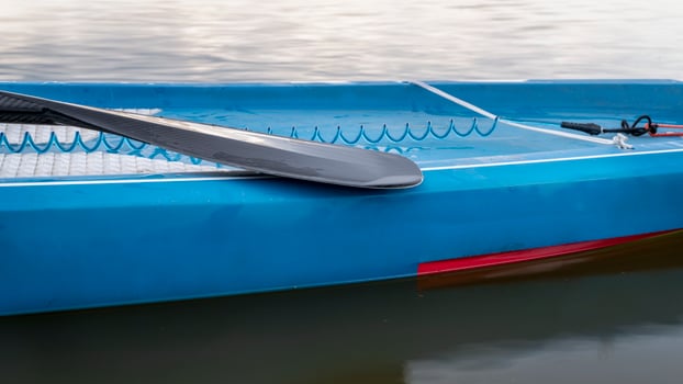 wet paddle and a coiled safety leash on a deck of stand up paddleboard photo