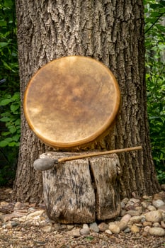 handmade, native American style, shaman frame drum covered by goat skin with a beater under an oak tree photo