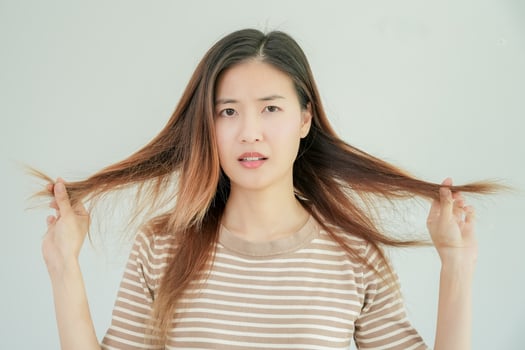 Asian woman very sad and upset looking at damaged hair, hair loss, hair thinning problem, vitamin deficiency, baldness, postpartum, biotin, zinc, menstrual or endocrine disorders, hormonal imbalance photo