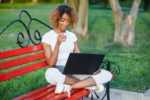 Portrait of african american woman with afro hairstyle sitting on the wooden bench outdoor and working on laptop photo