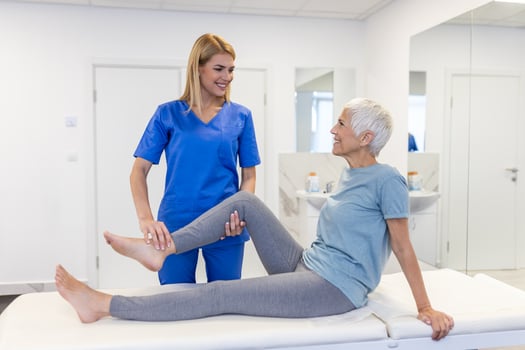 close up of female physiotherapist is helping senior elder woman stretching her hamstring and doing thigh or leg rehabilitation in exercise room - she is lying on massage bed photo