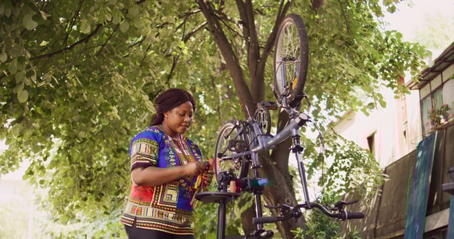 Young healthy black woman examining professional toolkit and repairing bicycle. Sporty female cyclist holding various specialized equipment for servicing damaged bike in home yard. photo