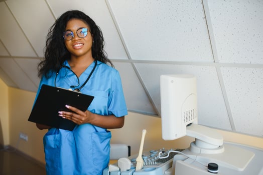 Young african-american female doctor in white coat using ultra ultrasound scanning machine and looking on the screen. African woman doctor working on modern ultrasound equipment. photo
