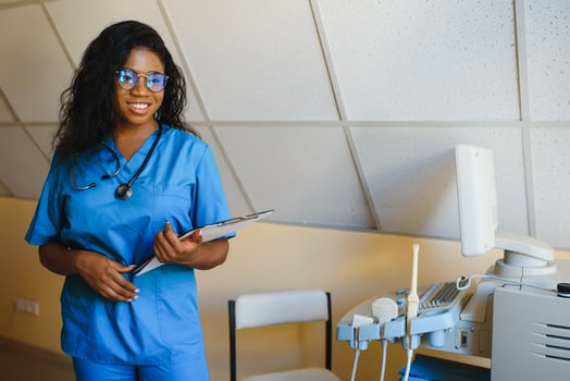 Young afro american female doctor standing in clinic office near modern ultrasound machine. photo