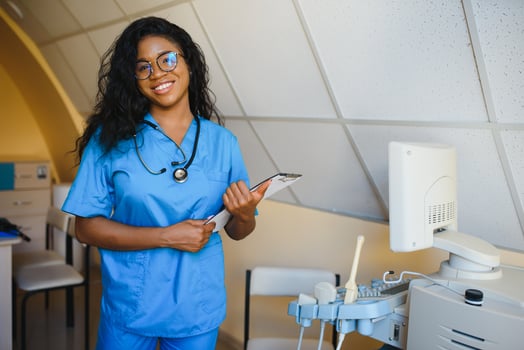 Young afro american female doctor standing in clinic office near modern ultrasound machine. photo