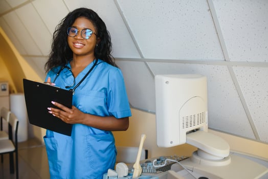 Young afro american female doctor standing in clinic office near modern ultrasound machine. photo