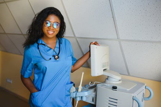 Young afro american female doctor standing in clinic office near modern ultrasound machine. photo
