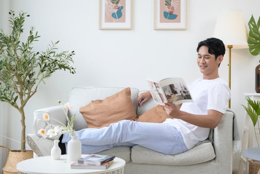 Happy asian man sitting on couch  reading a book in living room at home, relax time and lifestyle concept photo