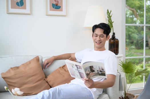 Happy asian man sitting on couch  reading a book in living room at home, relax time and lifestyle concept photo