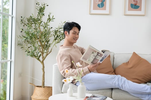Happy asian man sitting on couch  reading a book in living room at home, relax time and lifestyle concept photo