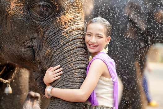 Beautiful rural Thai girl wear Thai northern traditional dress hug trunk of Asian elephant with blurred of water spray and any elephant background. photo