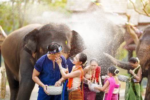 Young woman ware Thai traditional dress applies powder to a young man's cheek on an elephant splashing water background at Songkran festival. photo