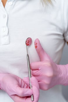 Dentist holds specific medical instruments for examining patient. Dental mirror with reflection of pained smile on finger with pink gloves. Dental care concept. photo