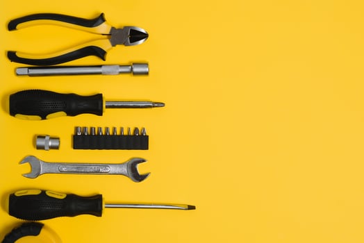 Yellow and black handy tools pilers and screwdriver isolated on yellow background. photo