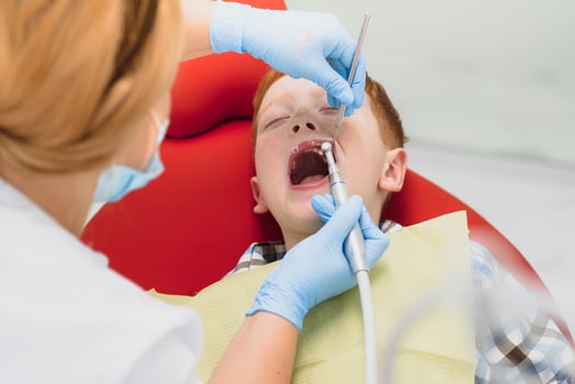 Pediatric dentist examining a little boys teeth in the dentists chair at the dental clinic photo