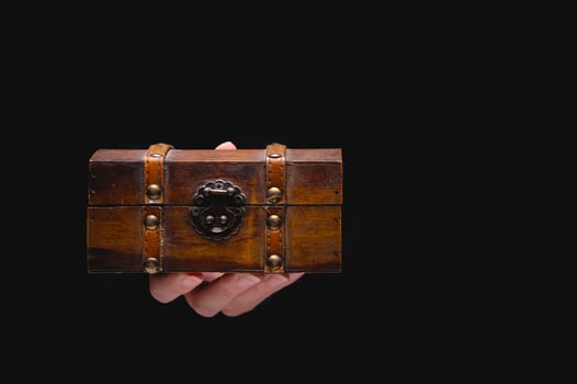 An old wooden box chest on a young female hand on a black background. Nice gift concept in gothic vintage style photo