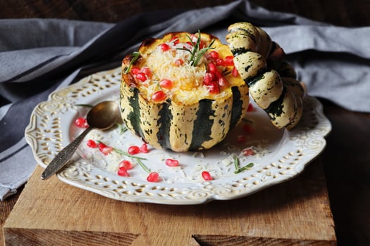 Pumpkin risotto served in a hollowed pumpkin. Baked pumpkin with cheese and pomegranate seeds on dark background. Selective focus photo