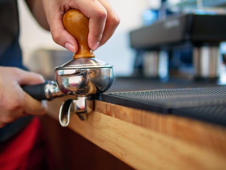 Hand of a barista holding a portafilter and a coffee tamper making an espresso coffee. Barista presses ground coffee using a tamper in a coffee shop photo