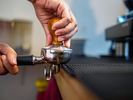 Hand of a barista holding a portafilter and a coffee tamper making an espresso coffee. Barista presses ground coffee using a tamper in a coffee shop photo