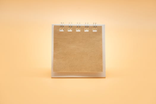 Blank calendar with brown paper isolated on orange background. Blank paper desk spiral calendar. close up of a blank recycle paper template. photo