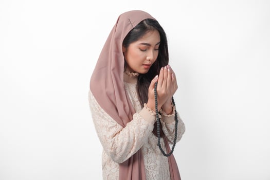 Beautiful Asian Muslim woman praying to God fervently, praying gesture with hands raised up and holding prayer bead. Ramadan and Eid Mubarak concept photo