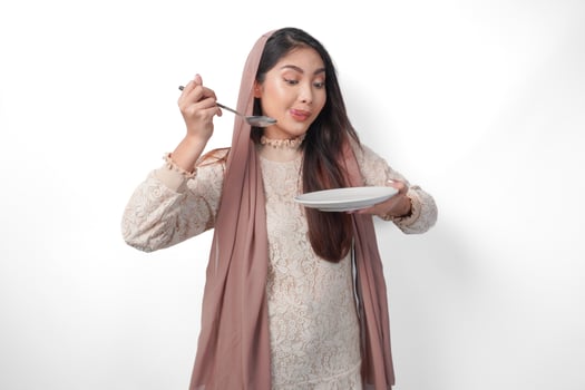 Portrait of a hungry Asian Muslim woman holding cutlery to eat or taste delicious dishes on the copy space over the plate, isolated white background photo