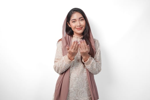 Religious Asian Muslim woman wearing veil headscarf with hands in praying gesture to God, standing over isolated white background. Ramadan and Eid Al Fitr concept photo