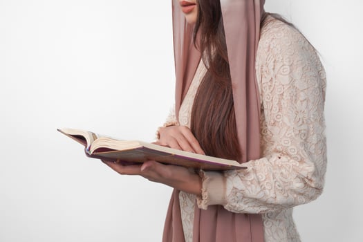 Close up portrait of Asian Muslim woman in headscarf veil hijab holding and reading Al Quran over isolated white background. Ramadan and Eid Mubarak concept. photo