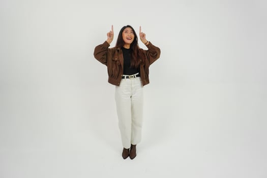 Happy Asian woman wearing casual clothes smiling while pointing up at a copy space, standing at isolated white background photo