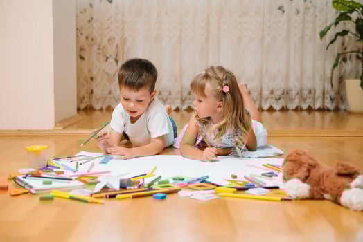Kids drawing on floor on paper. Preschool boy and girl play on floor with educational toys - blocks, train, railroad, plane. Toys for preschool and kindergarten. Children at home or daycare photo
