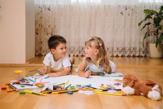 Kids drawing on floor on paper. Preschool boy and girl play on floor with educational toys - blocks, train, railroad, plane. Toys for preschool and kindergarten. Children at home or daycare photo