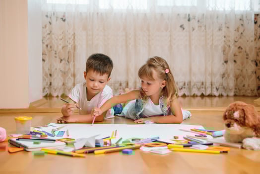 Kids drawing on floor on paper. Preschool boy and girl play on floor with educational toys - blocks, train, railroad, plane. Toys for preschool and kindergarten. Children at home or daycare photo