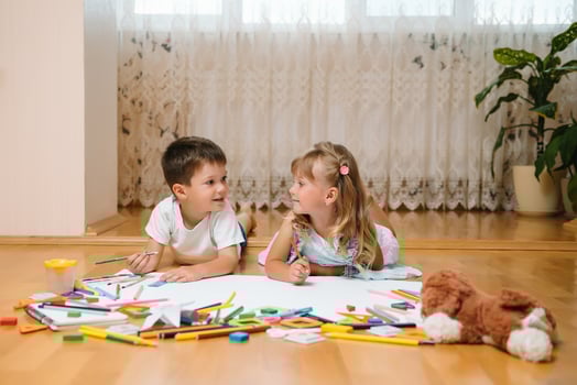 Kids drawing on floor on paper. Preschool boy and girl play on floor with educational toys - blocks, train, railroad, plane. Toys for preschool and kindergarten. Children at home or daycare photo