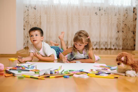 Kids drawing on floor on paper. Preschool boy and girl play on floor with educational toys - blocks, train, railroad, plane. Toys for preschool and kindergarten. Children at home or daycare photo