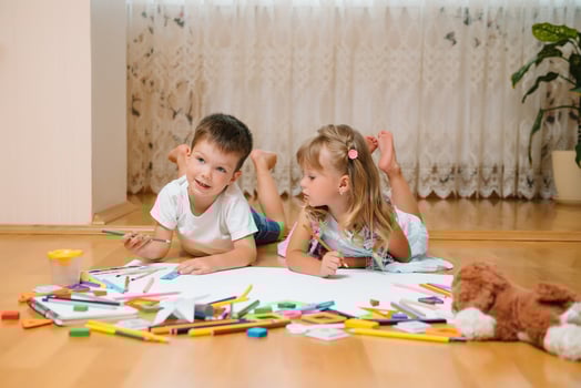 Kids drawing on floor on paper. Preschool boy and girl play on floor with educational toys - blocks, train, railroad, plane. Toys for preschool and kindergarten. Children at home or daycare photo