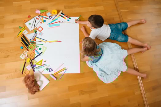 Kids drawing on floor on paper. Preschool boy and girl play on floor with educational toys - blocks, train, railroad, plane. Toys for preschool and kindergarten. Children at home or daycare. Top view. photo