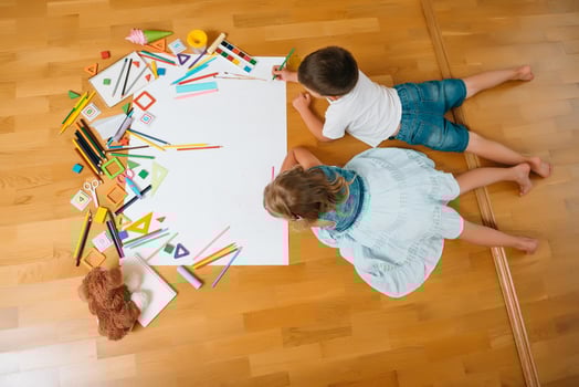 Kids drawing on floor on paper. Preschool boy and girl play on floor with educational toys - blocks, train, railroad, plane. Toys for preschool and kindergarten. Children at home or daycare. Top view. photo