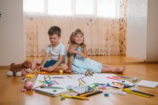 Kids drawing on floor on paper. Preschool boy and girl play on floor with educational toys - blocks, train, railroad, plane. Toys for preschool and kindergarten. Children at home or daycare photo