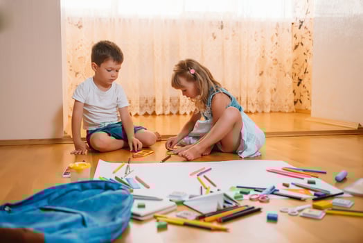 Kids drawing on floor on paper. Preschool boy and girl play on floor with educational toys - blocks, train, railroad, plane. Toys for preschool and kindergarten. Children at home or daycare photo