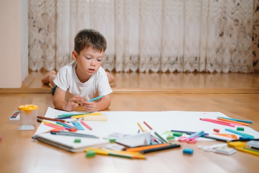 Kids drawing on floor on paper. Preschool boy and girl play on floor with educational toys - blocks, train, railroad, plane. Toys for preschool and kindergarten. Children at home or daycare photo