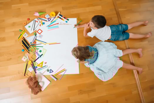 Kids drawing on floor on paper. Preschool boy and girl play on floor with educational toys - blocks, train, railroad, plane. Toys for preschool and kindergarten. Children at home or daycare. Top view. photo