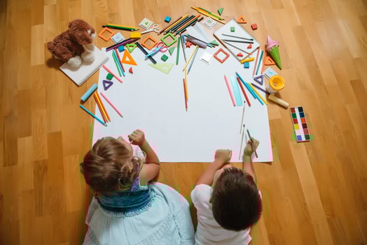 Kids drawing on floor on paper. Preschool boy and girl play on floor with educational toys - blocks, train, railroad, plane. Toys for preschool and kindergarten. Children at home or daycare. Top view. photo