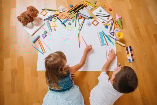 Kids drawing on floor on paper. Preschool boy and girl play on floor with educational toys - blocks, train, railroad, plane. Toys for preschool and kindergarten. Children at home or daycare. Top view. photo